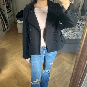 Svart skepparkavaj med knappar - Säljer en svart skepparkavaj med dubbelknäppning och bred krage. Jackan har långa ärmar och två fickor framtill. Materialet är tjockt och känns som ull, perfekt för kyliga dagar. Snygg och klassisk modell som är enkel att matcha med jeans eller kjol. Lite hårig då den legat i garderoben men rollar av innan jag postar💓💓