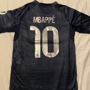 Real Madrid Mbappé matchtröja S - Snygg Real Madrid fotbollströja från Adidas i marinblått med silverfärgade detaljer och tryck. Mbappé och nummer 10 på ryggen. 