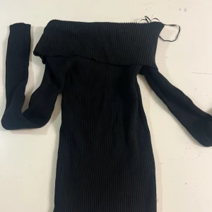 Svart ribbad offshoulder tröja XS - Svart ribbad klänning från Sister Knitwear i storlek XS. Modellen är offshoulder med långa ärmar och har en tight passform. Stickad struktur ger en cool och trendig vibe, perfekt för dig som gillar minimalistisk stil.
