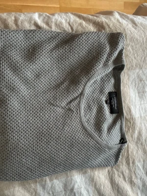 Grå tröja från Lindbergh - Säljer en grå tröja från Lindbergh i storlek L.  Tröjan har ett snyggt strukturerat mönster och rund hals. Perfekt för dig som gillar enkel och stilren design med lite extra textur. Långärmad och med ribbade muddar vid hals och nederkant.