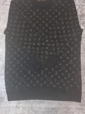 Svart Louis Vuitton sweatshirt XXL - Svart sweatshirt från Louis Vuitton i storlek XXL med ikoniskt monogrammönster över hela tröjan. Tröjan har rund hals och långa ärmar med ribbade muddar. Materialet är mjukt och känns lyxigt, perfekt för dig som gillar designerplagg med tydlig logga. Pris kan diskuteras vid snabb affär. Möjlighet för byten finns.