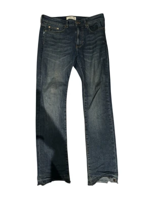 Blå jeans från Pier One - Snygga blå jeans från Pier One med klassisk femficksdesign och raka ben. Jeansen har en mörk tvätt med lätt slitning och kontrastsömmar. Perfekt för dig som gillar enkel och tidlös stil. Materialet är robust denim som håller länge.