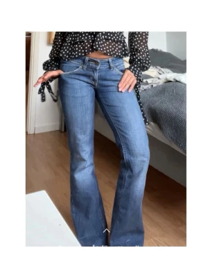 Lee vintage lågmidjade  bootcut jeans blå - Säljer ett par klassiska Lee vintage superlågmidjade jeans i blå tvätt med bootcut-snitt och låg midja. Jeansen har fem fickor, tydliga sömmar och Lee läderpatch bak i midjan. Perfekta för dig som gillar retrovibe och snygg passform. Midje: 36cm och innebenslängd: 72cm (Jenssen är uppklippta så passar en i petite längd (150-156cm)  🥰🥰