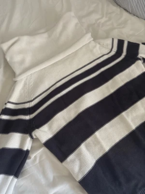 Randig polotröja från Newhouse - Säljer en stickad polotröja från Newhouse med breda svarta och vita ränder. Tröjan har lång ärm och krage som går att vika ner. Materialet är mjukt och skönt, perfekt för kyliga dagar eller en sommarkväll. 