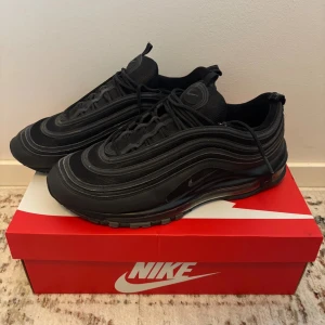 Nike Air Max 97 Svarta sneakers - Nike Air Max 97 sneakers i helsvart med vågiga linjer och reflekterande detaljer. Perfekta för dig som gillar streetstyle och sportig vibe. Passar bra till kalla säsonger. Slitage ses endast på yttersulan.