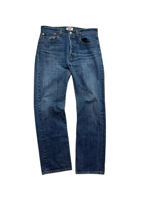 Levi's 501 blå jeans straight fit - Klassiska Levi's 501 jeans i blå tvätt med raka ben och normal passform. Jeansen har fem fickor, knappgylf och ikonisk läderpatch bak i midjan. Tillverkade i slitstarkt bomullsdenim med snygga kontrastsömmar. Perfekta för dig som gillar tidlös stil.