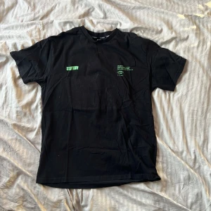 Svart t-shirt Stay High Black Squad XL - Svart t-shirt från Black Squad i storlek XL med grön text 'STAY HIGH' både fram och bak. T-shirten har rund hals, korta ärmar och är gjord i mjuk bomull. Snygg och chill stil med tryck som sticker ut. Perfekt till sommaren.