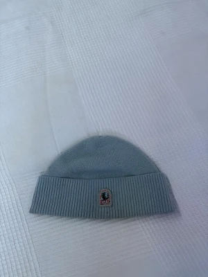 Parajumpers mössa - Säljer en stilren ljusgrå ribbstickad mössa från PJS med uppvikt kant och klassisk logga framtill. Perfekt accessoar för att hålla värmen och ge outfiten en clean vibe.