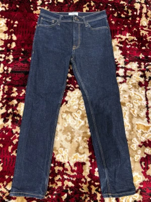 Mörkblå jeans från Produkt - Säljer ett par klassiska mörkblå jeans från Produkt med raka ben och snygga kontrastsömmar. Jeansen har fem fickor och stängs med knapp och dragkedja. Perfekta för dig som gillar en enkel och stilren look.