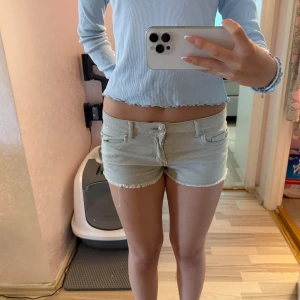 jeansshorts - Snygga jeansshorts med låg midja och fransig kant nertill. Klassisk femficksmodell med bälteshällor och knappstängning framtill. Perfekta för varma sommardagar och ger en avslappnad vibe.