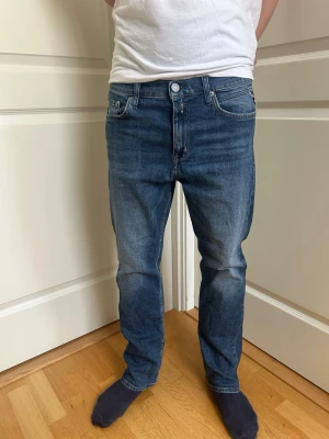 Blå jeans Replay Thad straight fit - Snygga blå jeans från Replay, modell Thad med klassisk femficksdesign och raka ben. Jeansen har en cool tvätt med lätt slitning på framsidan och bakfickor med Replay-logga. Passar dig som gillar en enkel och stilren look.