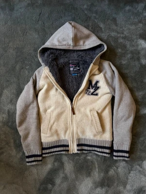 Beige teddyjacka - Vintage teddyjacka i beige med grå ärmar och mörkgrått fluffigt foder. Riktigt fet och varm med huva, dragkedja och två fickor. Broderad MZ 72-patch och ribbstickade muddar med svarta ränder. Ger vintage Hollister vibe.