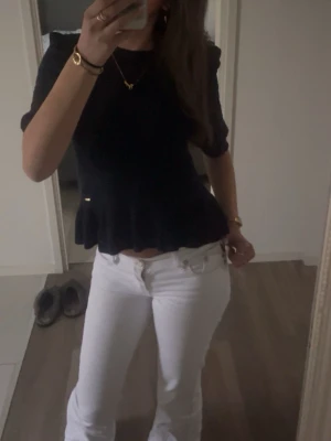 Mörkblå stickad blus med volang - Säljer en mörkblå stickad blus med korta ärmar och volangkant nedtill. Toppen har ett diskret mönster i stickningen och en rund halsringning. Perfekt att styla med både ljusa och mörka jeans för en cool look.