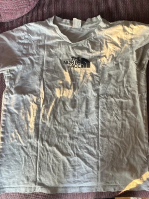 Vit t-shirt från The North Face - Säljer en vit t-shirt från The North Face med svart tryck på bröstet och ett stort statement-tryck på ryggen: 'Walls are meant for climbing'. Klassisk rund hals och korta ärmar, tillverkad i mjuk bomull. Perfekt för dig som gillar klättring och streetwear.