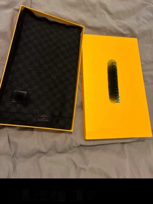 Louis Vuitton Haldsduk - Säljer en stilren väst från Louis Vuitton med klassiskt rutigt mönster i mörkgrå och svart ton. Västen har en diskret LV-logga framtill och är tillverkad i mjuk ull. Perfekt för dig som vill ha en exklusiv och tidlös look.