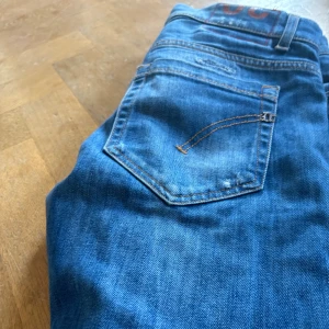 Blå skinny jeans från George, stl 30 - Säljer ett par blå skinny fit jeans från George i storlek 30. Jeansen har slitna detaljer och hål på benen för en cool, avslappnad look. Klassisk femficksmodell med orange sömmar och knappgylf. Perfekt för dig som gillar smal passform och streetstil.