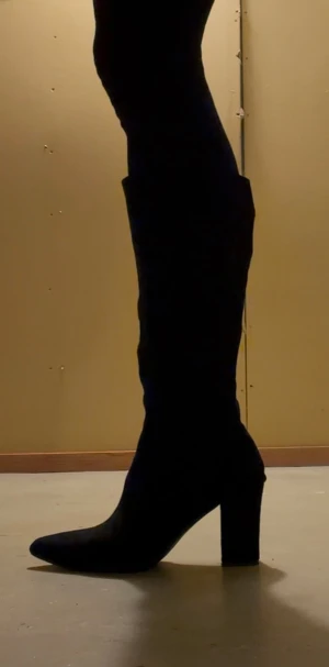 Svarta stövlar i fuskmocka, mycket fint skick! - Säljer ett par svarta stövlar i fuskmocka med hög klack 8cm och spetsig tå. De når upp under knät. Sula i syntetmaterial. Skaftvidd 40 cm. Strl 38. Mycket fint skick!