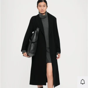 Svart lång kappa med bälte - Stilren svart lång kappa med klassisk krage och bälte i midjan. Kappan har rak passform, långa ärmar och slät yta. Perfekt för dig som gillar minimalistisk och tidlös stil. Materialet är ullblandning för extra värme. Den är lite nopprig då den är använd men i sin helhet i fint skick. Nypris 4 345kr