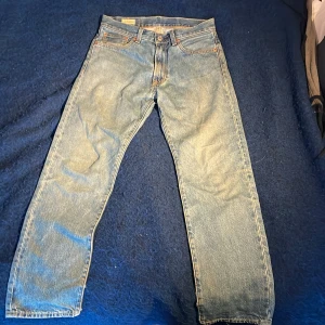 Levi's 501 ljusblå jeans straight fit - Klassiska Levi's 501 jeans i ljusblå tvätt med raka ben och normal passform. Jeansen har fem fickor, dragkedjagylf och den ikoniska läderpatchen bak i midjan. Tillverkade i slitstarkt bomullsjeans, perfekt för en avslappnad och tidlös look.