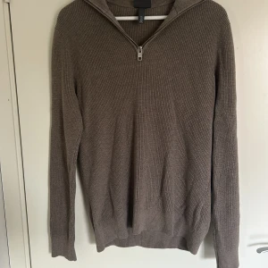Brun stickad half zip-tröja H&M - Säljer en brun ribbstickad tröja från H&M i slim fit-modell. Tröjan har lång ärm och en snygg half zip-dragkedja vid halsen. Perfekt för lager-på-lager och chill höst- eller vinterstil.