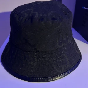 GG jumbo bucket hat - Säljer en svart jumbo bucket hat från GG med diskret GG-monogram över hela hatten. Hatten har en klassisk form med rund kulle och nedåtlutande brätte, samt en snygg kant i svart skinnimitation. Perfekt accessoar för en trendig streetstyle-look.