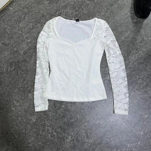 Vit spetsärmad topp från SHEIN - Säljer en vit topp från SHEIN i storlek XS. Toppen har långa ärmar i genombruten spets och en snygg v-ringad halsringning. Kroppen är i slät bomullsmix och modellen är figurnära. Perfekt för dig som gillar romantiska detaljer och stilren look.