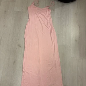 Ljusrosa långklänning Gina Tricot - En enkel och stilren ljusrosa långklänning från Gina Tricot. Klänningen är ärmlös och har en rak, smal passform. Tillverkad i mjuk bomull som känns skön mot huden. Perfekt för varma dagar när du vill ha något bekvämt och snyggt.