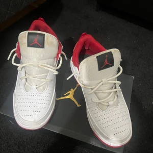Vita och röda Nike Jordan sneakers - Säljer ett par fräscha Nike Jordan sneakers i vitt och rött med klassisk Jumpman-logga på plösen. Skorna har perforerad tå, röda detaljer runt häl och foder samt vit snörning. Snygg och sportig design som sticker ut, perfekt för dig som gillar streetstyle.