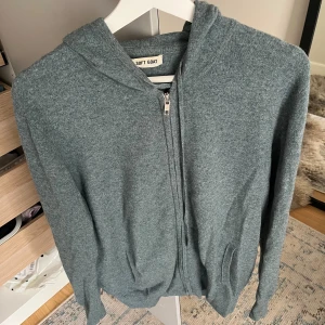 Grå hoodie i kashmir från Soft Goat - Mysig grön/blå hoodie från Soft Goat i kashmir. Tröjan har dragkedja framtill, huva och två fickor och  materialet är supermjukt.