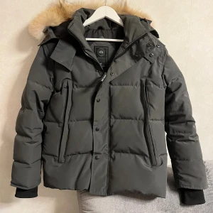 Svart pufferjacka från Canada Goose XS - Säljer en svart pufferjacka från Canada Goose i storlek XS. Jackan har en fluffig huva med beige fuskpäls, dragkedja och knappar framtill samt två stora fickor. Perfekt för kalla vinterdagar och riktigt snygg passform. Skick 8/10 knappen längst ner har åkt av men inget man tänker på. Priset är inte hugget i sten så kom med förslag