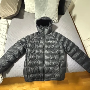 Svart dunjacka Peak Performance M - Säljer en svart dunjacka från Peak Performance i storlek M. Jackan har huva, dragkedja framtill och två sidofickor. Den är quiltad och har en clean, sportig look med diskret logga på bröstet. Perfekt för kalla dagar när du vill hålla stilen. Använd ett fåtal gånger