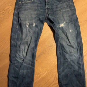 Levi's 549 blå jeans 33x32 - Säljer ett par vintage Levi's 549 jeans i klassisk blå denim med slitningar och trasiga detaljer på låren. Jeansen har rak passform och femficksdesign.