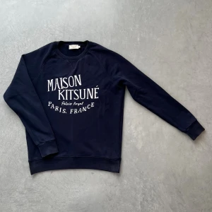Mörkblå sweatshirt Maison Kitsuné - Snygg mörkblå sweatshirt från Maison Kitsuné med vit tryckt text på bröstet. Tröjan har rund hals, långa ärmar och ribbade muddar. Perfekt för dig som gillar stilren streetwear med fransk touch.