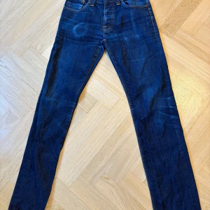 Mörkblåa Nudie Jeans - Säljer ett par mörkblåa nudie jeans i storleken W29 L34, jeansen är i modellen slim och är i bra skick med en liten defekt på höger ficka. De är mörkblåa med orangea detaljer och är riktigt stilrena.