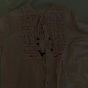 Ljusrosa Odd Molly blus med knyt - Supersöt ljusrosa blus från Odd Molly med smockad framsida, broderad logga och knytband i midjan. Knappar framtill och fina detaljer som ger en romantisk vibe. Perfekt för dig som gillar unika plagg med lite extra känsla. Inte andvänd! 