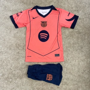 Barça Lamine Yamal fotbollströja Nike - Säljer en FC Barcelona fotbollströja med Lamine Yamal och nummer 10 på ryggen. Tröjan är korallrosa med mörkblå detaljer, korta ärmar och V-ringad krage. Tryck med Spotify och UNHCR-logga, samt tillhörande mörkblå shorts med klubbmärke. Perfekt för dig som älskar Barça.