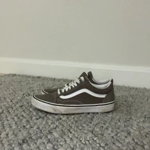 Grå Vans Old Skool sneakers - Säljer ett par klassiska Vans Old Skool sneakers i brun mocka och canvas med vita detaljer och snörning. Skorna har den ikoniska vita sidolinjen och platt sula. Perfekta för en avslappnad streetstyle-look. Anvönad bara et få tal gånger priset går stt diskutera ☺️