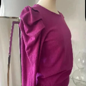 stickad tröja med volangärmar  - Snygg stickad tröja med långa ärmar och coola volangdetaljer på axlarna. Tröjan har rund halsringning och ribbad kant nedtill för en schysst passform. Perfekt för dig som vill sticka ut lite extra med din stil. Färgen är cerise 