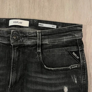 Replay Anbass svarta skinny jeans - Svarta Replay Anbass jeans med slitna detaljer och skinny passform. Jeansen har klassisk femficksdesign, dragkedjegylf och tydliga slitningar framtill för en cool, använd look. Märkeslapp på fickan och bak. Perfekta för dig som gillar streetstyle.