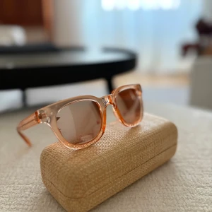 Transparanta orange solglasögon från Oysho - Snygga solglasögon från Oysho med transparent orange båge och matchande tonade glas. Klassisk, något fyrkantig form som ger en cool vibe. Perfekta för att lyfta din stil under soliga dagar. Kommer med ett stilrent fodral.