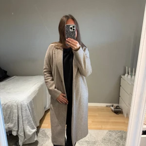 Beige kappa från Zara - Säljer en snygg beige kappa från Zara med klassisk krage och enkel knappstängning framtill. Kappan är perfekt för hösten samt lättare vintrar. Kappan håller värmen väldigt bra då den är i lite tjockare och material samt en lång modell. Kappan är köpt i mars och är använd ett par fä gänger men kommer tyvärr inte till användning denna hosten.