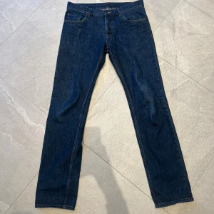 Prada jeans tight fit mörkblå - Snygga mörkblå jeans från Prada med tight fit. Klassisk femficksmodell med raka ben och diskreta detaljer. Jeansen har tydliga kontrastsömmar och metallknapp med Prada-logga. Perfekta för dig som gillar stilrena och exklusiva jeans.