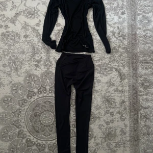 Träningsset - Svarta leggings från Gymshark och träningströja från Ronhill - Säljer ett par svarta leggings från Gymshark med hög midja och snygg omlott-detalj framtill. De är tillverkade i ett stretchigt som sitter tight och är perfekta för träning. Diskret Gymshark-logga på höften. Plaggen har ej använts tidigare, endast provats.