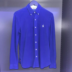 Blå skjorta från Ralph Lauren - Säljer en snygg blå skjorta från Ralph Lauren med klassisk krage och vita knappar. Skjortan har det ikoniska broderade polospelar-loggan på bröstet och är gjord i ett lätt mesh-material. Perfekt för dig som gillar stilrena och tidlösa plagg. 8/10 skick och har knappt andvänts. Har man några frågor eller funderingar är det bara att höra av sig 👍