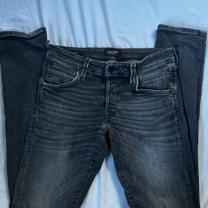 Jack & Jones Slim Glenn svarta jeans - Snygga svarta jeans från Jack & Jones, modell Slim Glenn. Jeansen har en slim passform, klassisk femficksdesign och diskreta slitningar för en cool look. Tillverkade i stretchigt jeanstyg för extra komfort. !!OBS!! Byxorna har en defekt längs ner vid vänstra häl, se bild! Storlek W30 L34