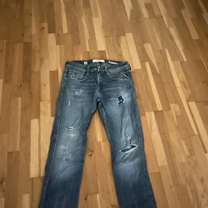 Replay Anbass slitna blå jeans - Säljer ett par Replay Anbass slim fit jeans i blå denim med slitningar och hål för en cool, avslappnad look. Klassisk femficksmodell med läderpatch bak i midjan och snygga detaljer. Perfekta för dig som gillar streetstyle.
