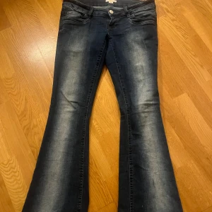 Mörkblå bootcut jeans med slitningar - Snygga mörkblå jeans med bootcut-modell och ljusa slitningar längs benen. Klassisk femficksdesign och låg midja. Jeansen har en markerad utställd passform nertill och är tillverkade i stretchigt denimtyg för extra komfort.