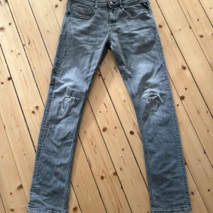Grå slitna jeans från Replay - Grå jeans från Replay med slitningar. Skön slimfit modell med stretch. Jeansen har en ljusgrå tvätt och är tillverkade i bomullsdenim. Perfekta för en avslappnad stilren stil. Byxorna är knappt använda då jag köpt andra. 