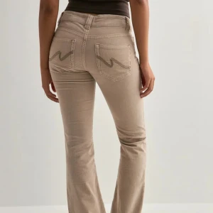 Beiga bootcut manchesterbyxor - Snygga beiga manchesterbyxor med bootcut-snitt och klassiska fickor bak med broderad detalj. Byxorna har låg midja och är tillverkade i mjukt manchestertyg som ger en retrovibe. Perfekta att styla med sneakers eller boots för en chill look.