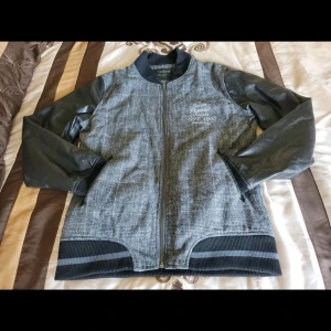 Grå rutig bomberjacka med skinnärmar - Snygg grå bomberjacka från Blend med rutigt mönster och svarta skinnärmar. Jackan har dragkedja framtill, ribbade muddar och quiltat foder. Perfekt för dig som vill ha en stilren och modern look.